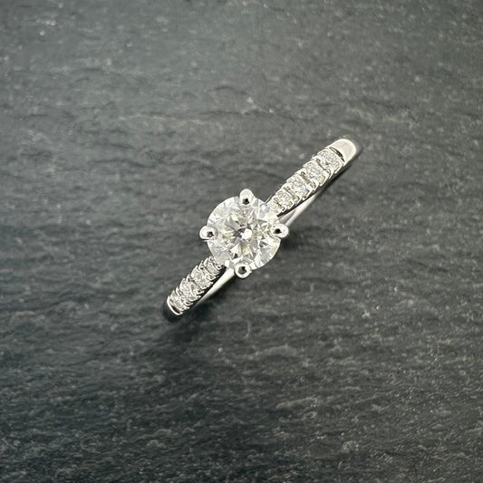 Pre-Owned: Platinum round brilliant cut diamond solitaire ring with diamond set shoulders.